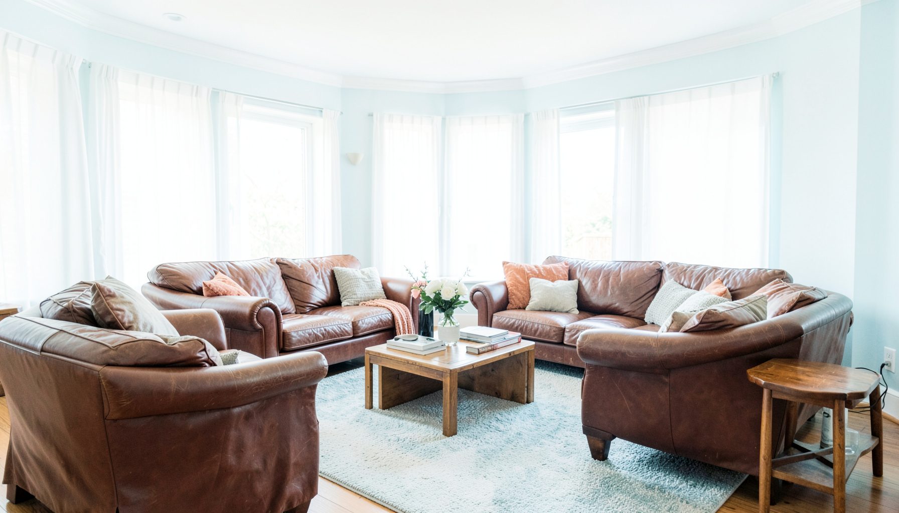 A spacious living room with rich brown leather sofas and armchairs, warm lighting, and wooden side tables