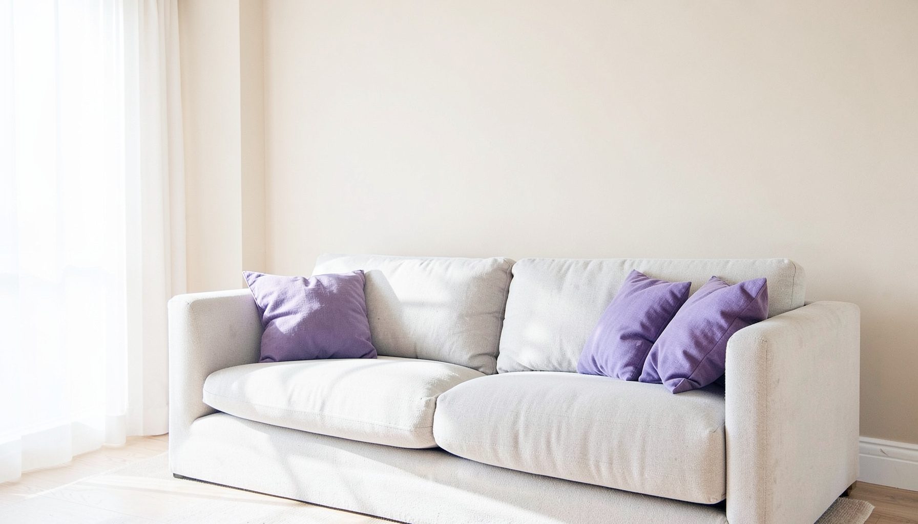 A serene living room with beige walls, purple accent cushions, and a plush neutral sofa